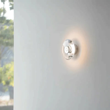 Applique murale en cristal diffusant un halo lumineux ambré sur un mur blanc près d'une fenêtre