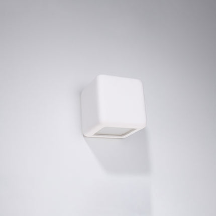 Applique cube céramique blanche fixée sur un mur clair, éclairage bidirectionnel eteint