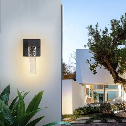 Applique murale cristal à bulles allumée sur un mur blanc près d'un jardin au coucher du soleil