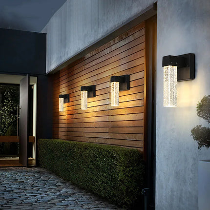 Appliques murales cristal alignées le long d'un mur en bois éclairant une entrée de terrasse le soir
