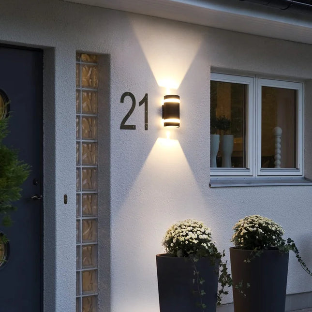 Applique murale extérieure cylindrique noire éclairant une façade près d'un numéro de maison