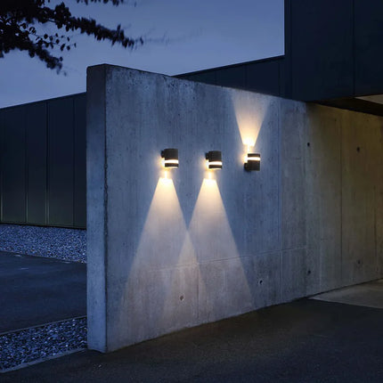 Trois appliques murales extérieures cylindriques noires sur un mur en béton la nuit