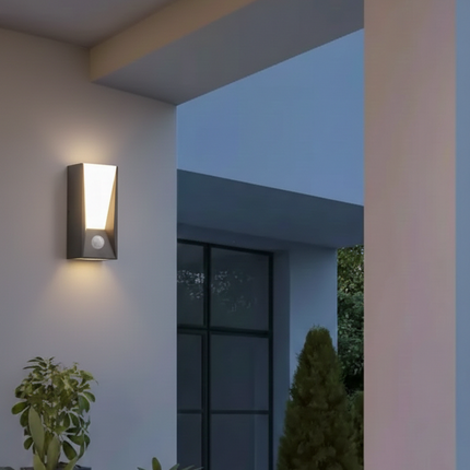 Applique murale extérieure LED gris anthracite avec détecteur allumée sur une façade près d'une entrée le soir