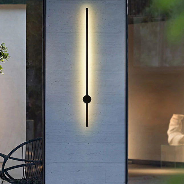 Applique extérieure linéaire noire diffusant une lumière chaude sur un mur de terrasse au crépuscule