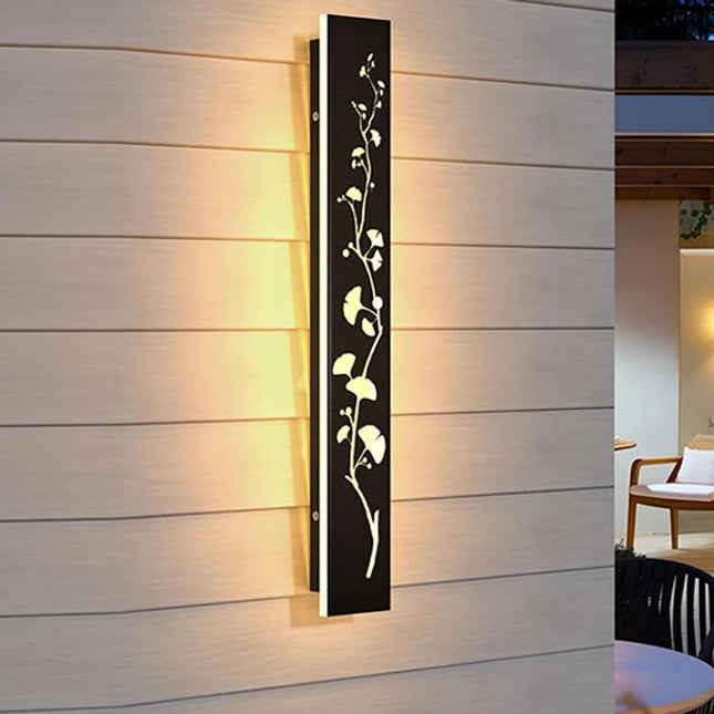 Applique murale extérieure noire à motif feuillage ajouré et LED allumée sur une façade en bois