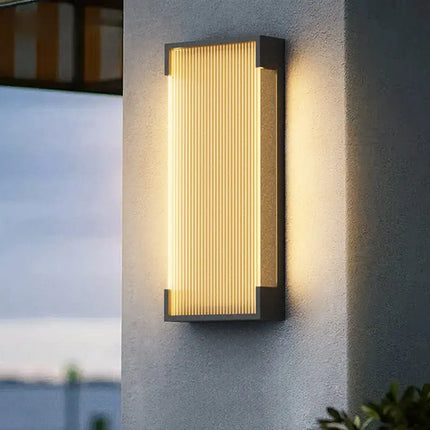 Applique murale extérieure solaire en aluminium noir à diffuseur cannelé, allumée sur une façade grise