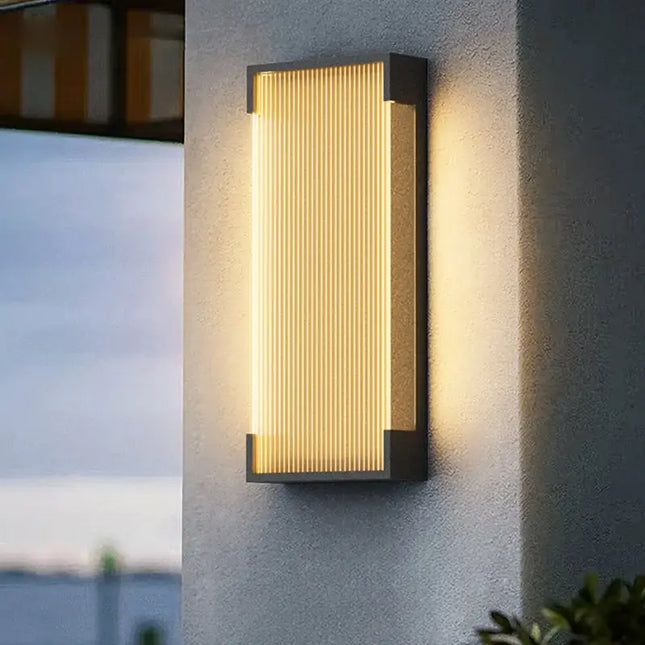 Applique murale extérieure solaire en aluminium noir à diffuseur cannelé, allumée sur une façade grise