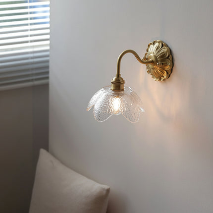 Applique murale fleur en verre fumé et laiton doré allumée, vue d'angle sur un mur blanc