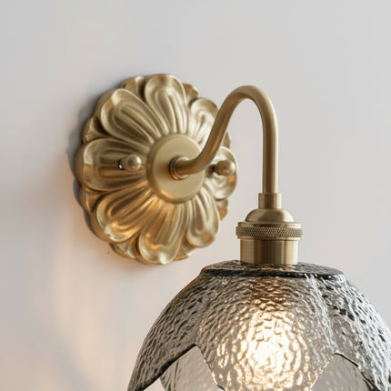 Détail des pétales de verre texturé fumé et de la rosace en laiton doré de l'applique murale fleur
