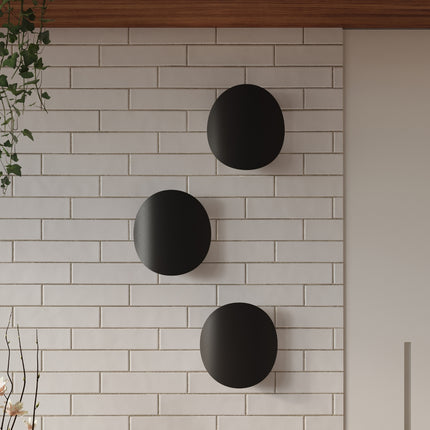 Composition de trois appliques galet noir mat sur un mur de briques blanches
