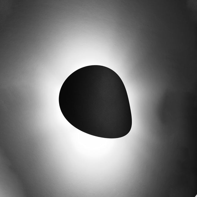 Applique galet noir mat allumee diffusant un halo de lumiere indirecte sur le mur