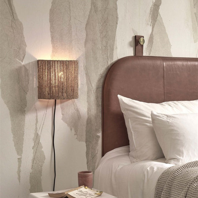 Lit Iguazu wall light above a bedside table, brown leather headboard
