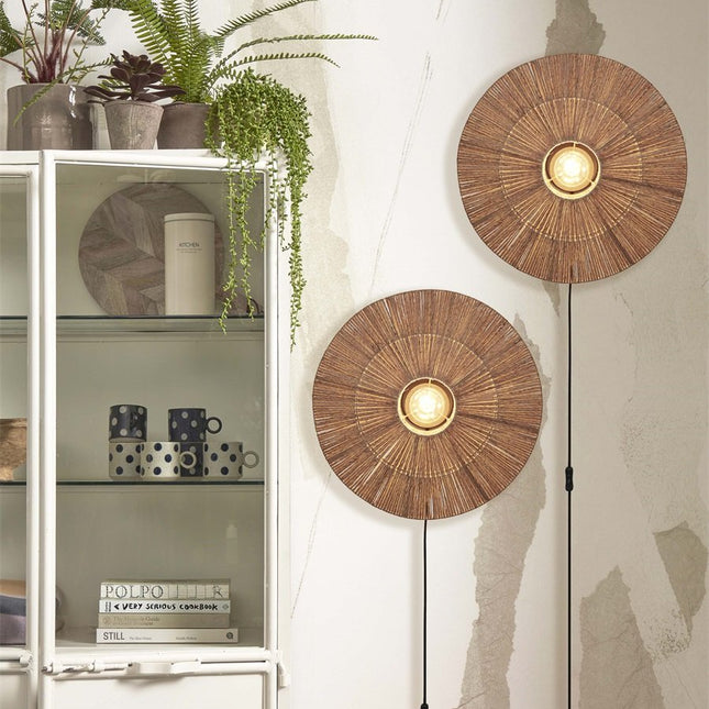 Two woven jute Iguazu wall lights mounted on the wall next to a shelf with green plants