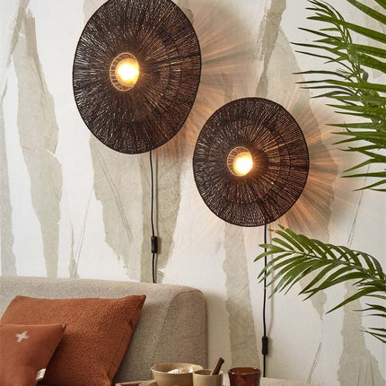 Zwei leuchtende Wandleuchten Iguazu aus geflochtener schwarzer Jute über einem beigen Sofa mit Terrakotta-Kissen