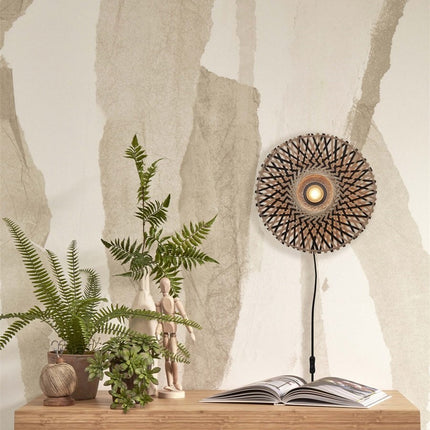 Applique murale Kalimantan en bambou tressé allumée au-dessus d'une console en bois avec plantes vertes