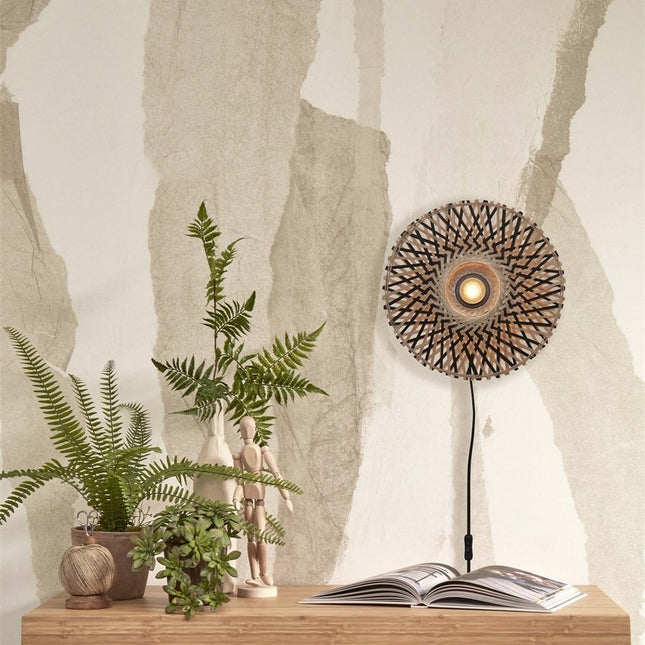 Applique murale Kalimantan en bambou tressé allumée au-dessus d'une console en bois avec plantes vertes