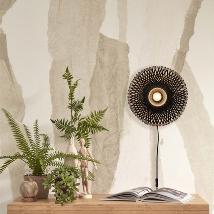 Applique murale Kalimantan en bambou tressé noir allumée au-dessus d'une table en bois avec plantes