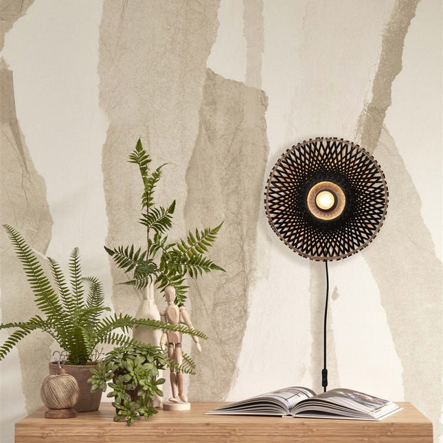 Applique murale Kalimantan en bambou tressé noir allumée au-dessus d'une table en bois avec plantes