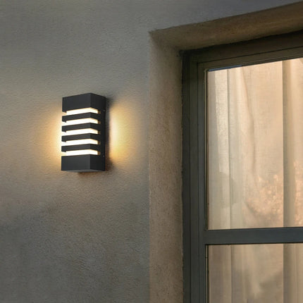 Applique murale LED anthracite diffusant un halo chaud sur un mur en crépi près d'une fenêtre