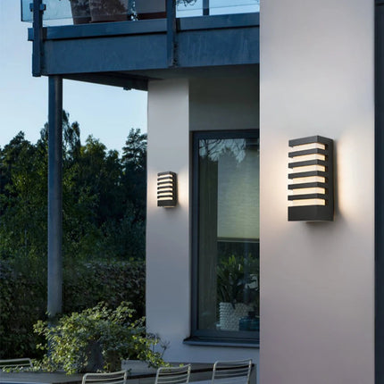 Applique murale LED anthracite allumée sur un mur blanc de terrasse à la tombée de la nuit