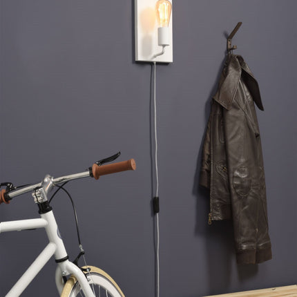Applique murale Madrid blanche allumée dans une entrée grise près d'un vélo et d'un porte-manteau
