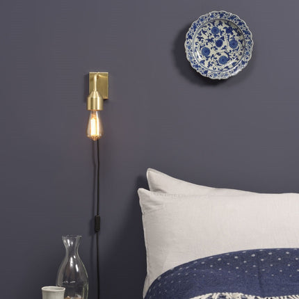Applique murale Madrid dorée installée au-dessus d'un chevet dans une chambre aux tons bleu nuit