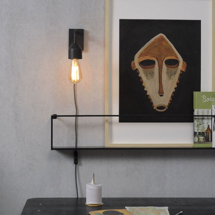 Applique murale Madrid en fer noir avec ampoule à filament, fixée au-dessus d'une étagère métallique dans un salon