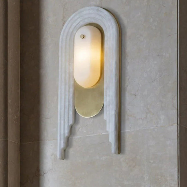 Applique murale en marbre et cuivre doré posée sur un mur de pierre claire, halo de lumière chaude
