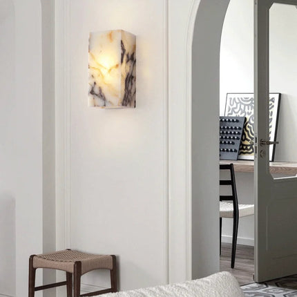 Applique en marbre naturel éclairant un mur d'entrée près d'une porte arquée, ambiance douce et feutrée