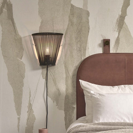 Applique murale Merapi en bambou noir installée en tête de lit, à côté d'une tête de lit en cuir dans une chambre cosy