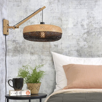 Applique murale Palawan en bambou tressé noir et naturel, bras articulé, installée au-dessus d'une table de chevet