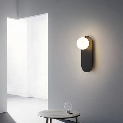 Applique murale pilule en fer noir et globe opalin allumée dans un intérieur épuré