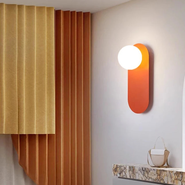 Applique murale pilule en fer orange et globe opalin dans une entrée aux tons chauds