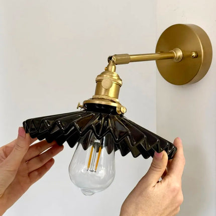Applique murale à abat-jour plissé en céramique noire et bras laiton doré, tenue à la main avec ampoule à filament