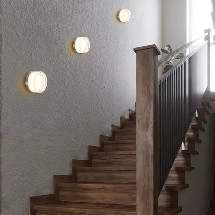 Trois appliques rondes en acrylique fumé rythmant le mur d'un escalier en bois