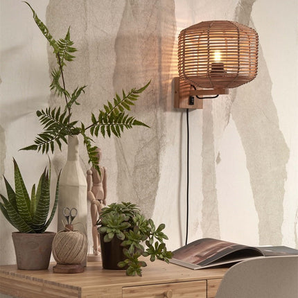 Applique murale Tanami en rotin tressé naturel allumée au-dessus d'un bureau en bois avec plantes vertes