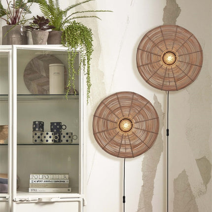 Tanami woven rattan wall lights switched on near a glass-fronted bookcase and green plants
