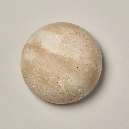Applique murale ronde en travertin naturel beige posée sur un mur clair, effet lune minéral