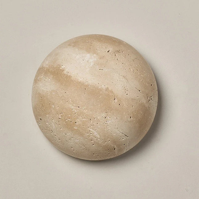 Applique murale ronde en travertin naturel beige posée sur un mur clair, effet lune minéral