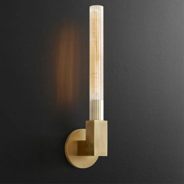 Applique murale tube en verre strié finition cuivre allumée sur un mur foncé, lumière chaude