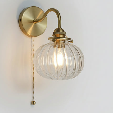 Détail du globe en verre cannelé transparent d'une applique murale dorée avec ampoule à filament