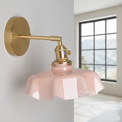 Applique murale en verre festonné rose et laiton doré posée sur un mur clair près d'une fenêtre
