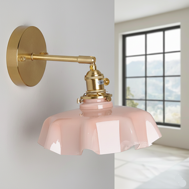 Applique murale en verre festonné rose et laiton doré posée sur un mur clair près d'une fenêtre