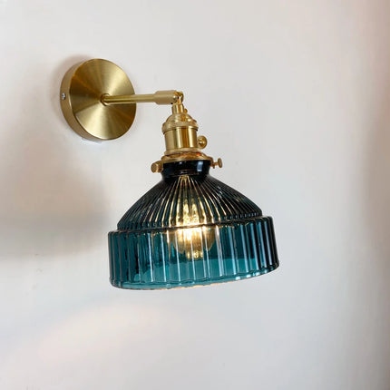Applique murale en verre strié bleu canard et laiton doré allumée sur un mur clair