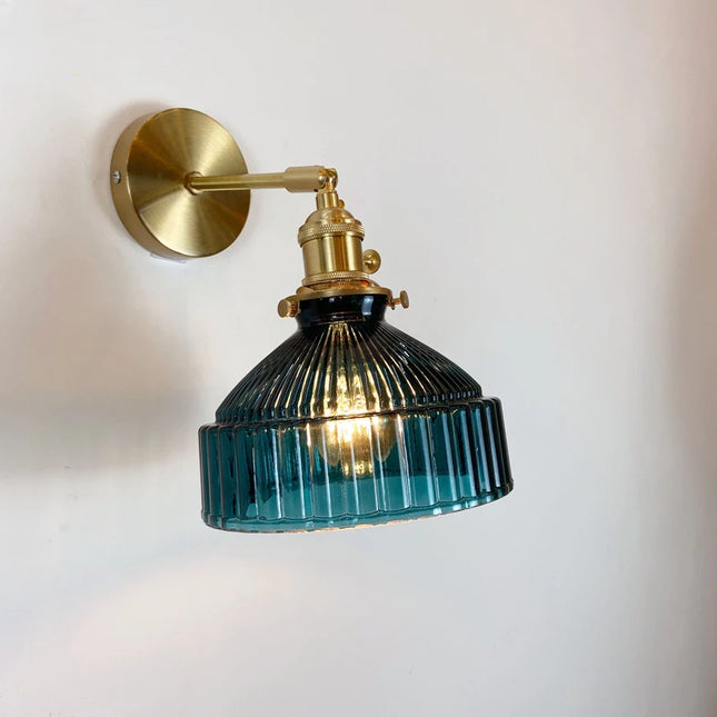 Applique murale en verre strié bleu canard et laiton doré allumée sur un mur clair
