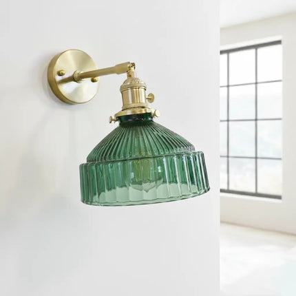 Applique murale en verre strié vert et laiton doré posée sur un mur blanc près d'une fenêtre