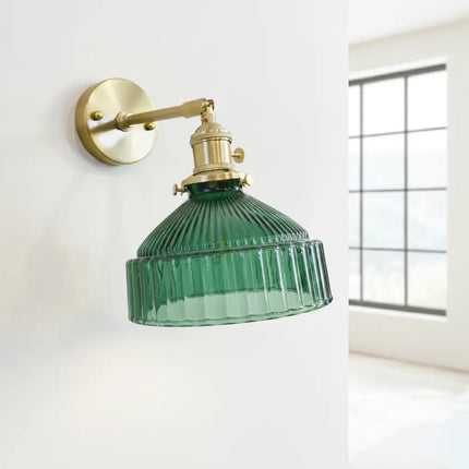 Applique murale vintage en verre vert strié et bras laiton orientable sur un mur clair lumineux