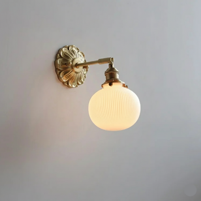 Applique murale vintage à globe en verre opalin strié et bras orientable en laiton doré, allumée sur un mur clair