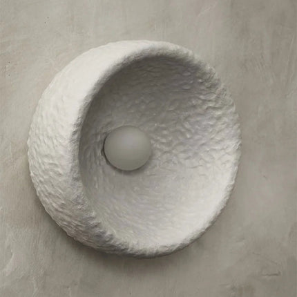 Gros plan d'une applique Wabi-Sabi allumée montrant la coupe en résine texturée effet stuc