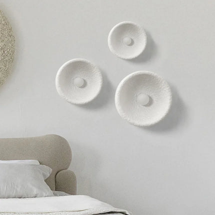 Trois appliques Wabi-Sabi blanches texturées disposées sur un mur clair près d'un lit